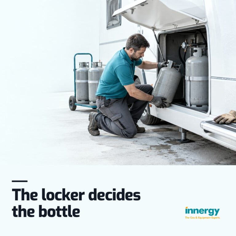 A worker in a teal polo kneels at a white caravan's open gas locker, lowering a second grey cylinder in, with the words "The locker decides the bottle" set on it