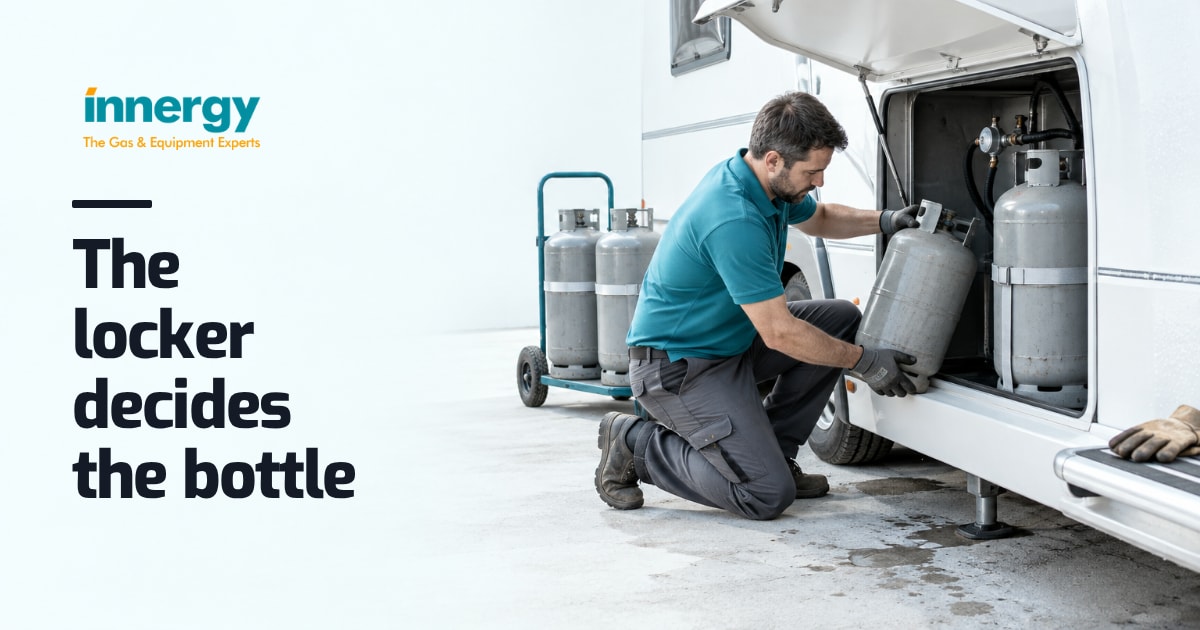 A worker in a teal polo kneels at a white caravan's open gas locker, lowering a second grey cylinder in, with the words "The locker decides the bottle" set on it